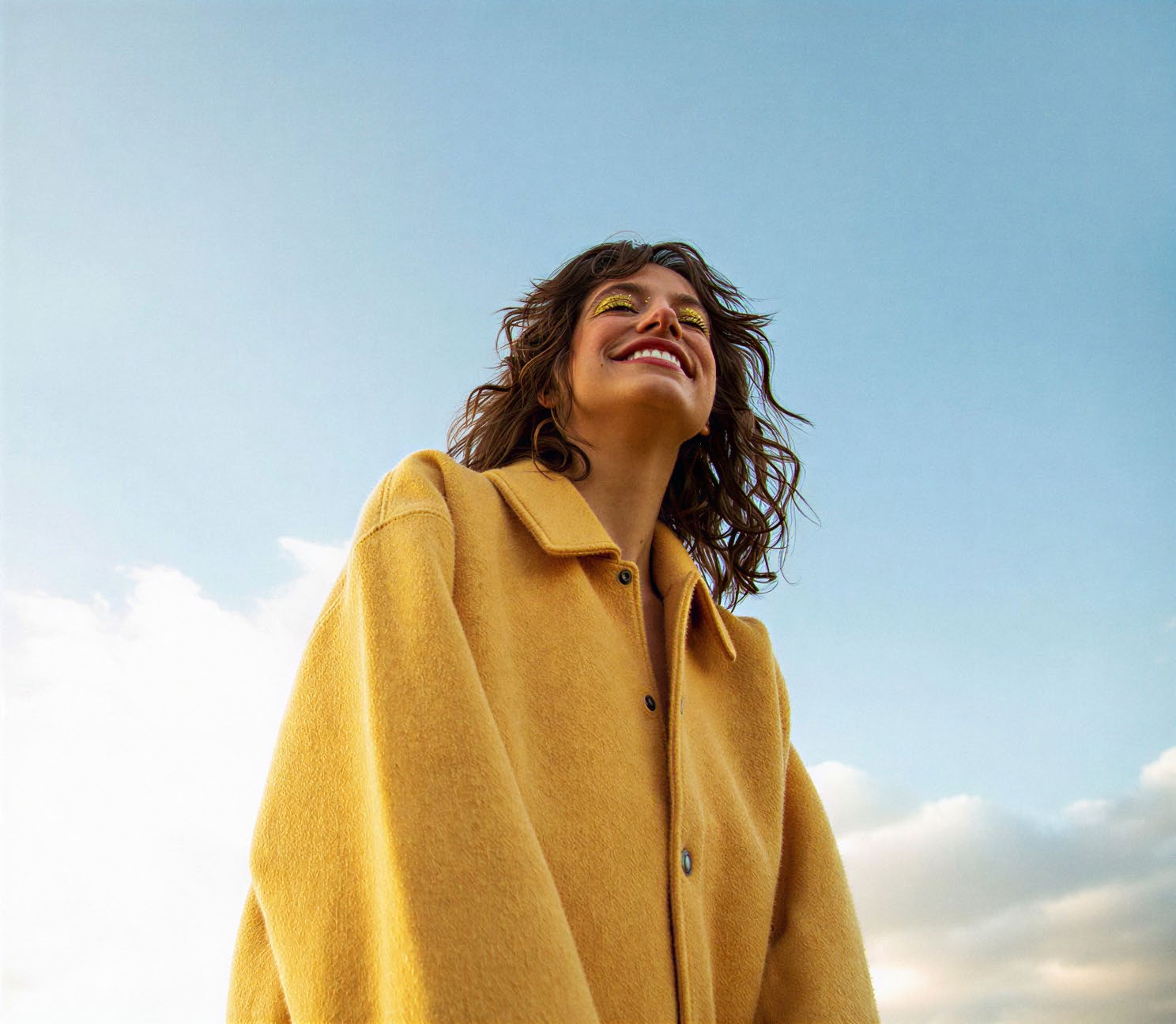 Mulher de casaco amarelo sorrindo sob céu azul